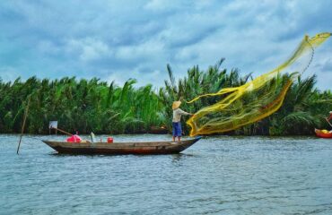 Sustainable Fishing – Blue Economy Vision Fisherman casting a net from a wooden boat in a coastal ecosystem, illustrating blue economy activities and sustainable marine livelihoods