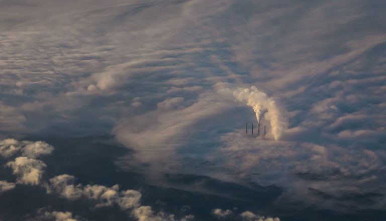 Aerial view of industrial smokestacks emitting CO2 into the atmosphere – a challenge that Climate Positive strategies aim to solve by removing emissions and restoring balance.