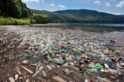 Plastic pollution covering a river with bottles and debris surrounded by forested hills